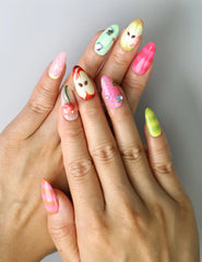 Hand model wearing medium almond nails in red and green with cartoon-style apple slices and a raised worm charm