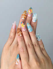 Hand model wearing almond-shaped press-on nails with pink floral art, starfish embellishments, and seashell-inspired texture