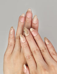 Hand wearing Naillover Blush Amber Grace handmade press on nails in peach and beige marble with chic gold details.