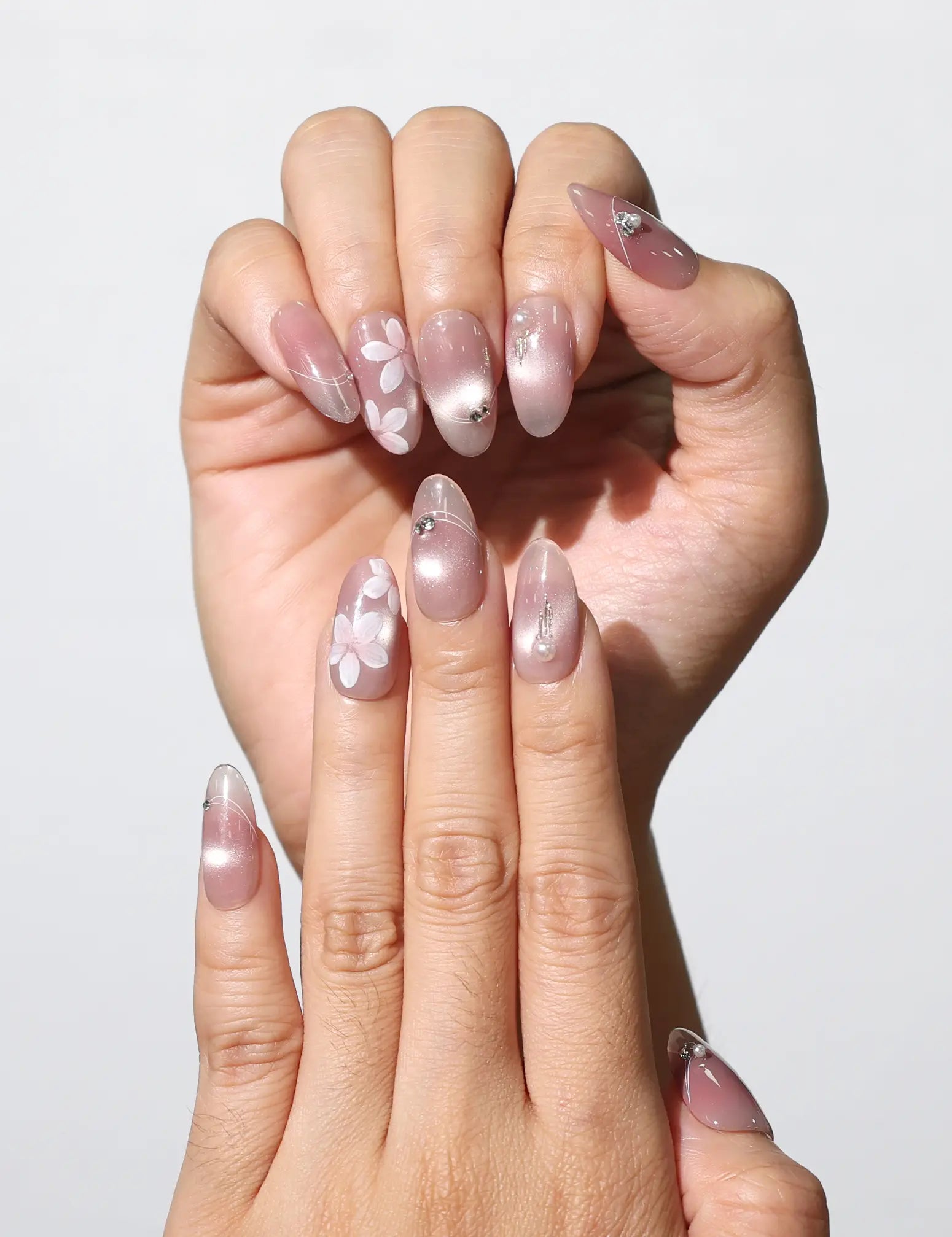 Fingers adorned with Blush Blossom Sparkle Singapore press on nails, showcasing floral and metallic details under soft lighting.