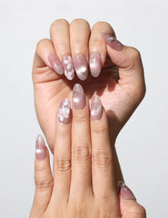 Fingers adorned with Blush Blossom Sparkle Singapore press on nails, showcasing floral and metallic details under soft lighting.