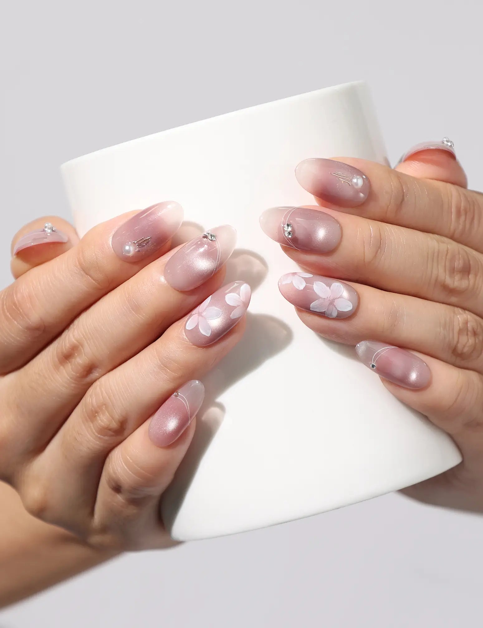 Hand holding a white coffee cup while wearing Blush Blossom Sparkle Singapore press on nails with delicate floral and metallic accents.