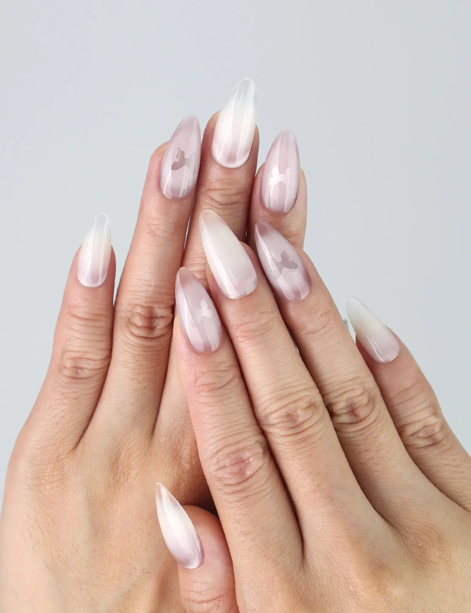 Hand model wearing pink almond-shaped press-on nails with soft white ombré and delicate butterfly accents