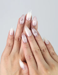 Hand model wearing pink almond-shaped press-on nails with soft white ombré and delicate butterfly accents