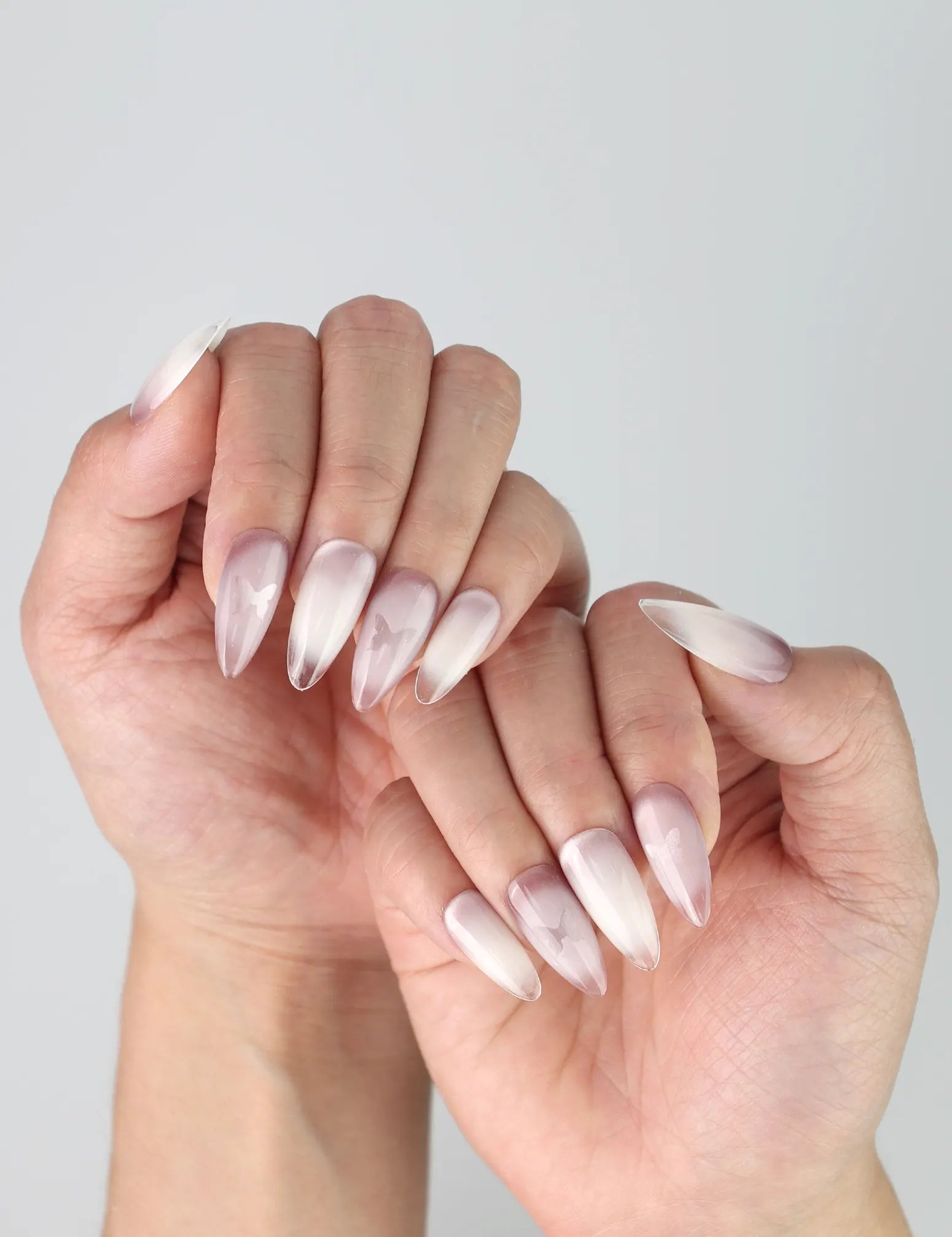 Side view of elegant press-on nails with a natural pink-to-white fade and sparkly butterfly details