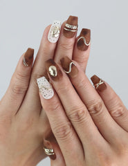 Hand wearing Naillover Caramel Luxe press on nails, showing swirl patterns and warm tones in natural lighting.