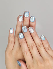 Hand wearing Naillover Celestial Blue handmade press on nails with shimmering blue swirls and glitter details.