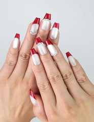 Hand model wearing crimson red coffin-shaped press-on nails with ombré fade to sparkling silver glitter tips