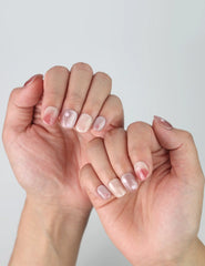 Fingers fanned out to display Naillover’s short squoval press ons with minimal nude tones and pink flower accents