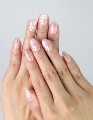 Hand model wearing oval-shaped press-on nails in soft pink with sculpted 3D floral accents