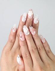 Hand model wearing medium pink oval press-on nails with 3D flowers, sparkly rhinestones, and heart charms