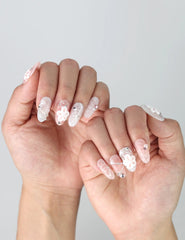 Side view of medium oval nails with dimensional floral nail art, rhinestones, and glossy pink base