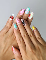 Hand model wearing medium almond press-on nails with soft pastel pink and blue gradients, cartoon cat prints, and stars