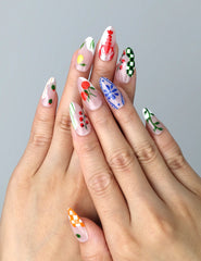 Hand model wearing almond-shaped press-on nails with delicate pastel florals, cherries, and daisy accents