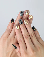 Hand gesture showcasing black handmade press on nails with intricate white and gold floral art, golden leaves, and rhinestone accents by Naillover