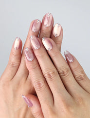 Hand model wearing short pink press-on nails with mauve-to-rose gradient, chrome shimmer, and gem details
