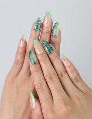 Hand model wearing nude and green short almond nails with gold foil and detailed tropical leaf nail art