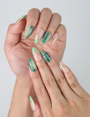 Close-up of handmade press-on nails in earthy nude and sage tones with palm leaf designs and shimmering gold accents