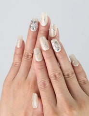 Hand model wearing short square ivory press-on nails with foil-like silver flower details