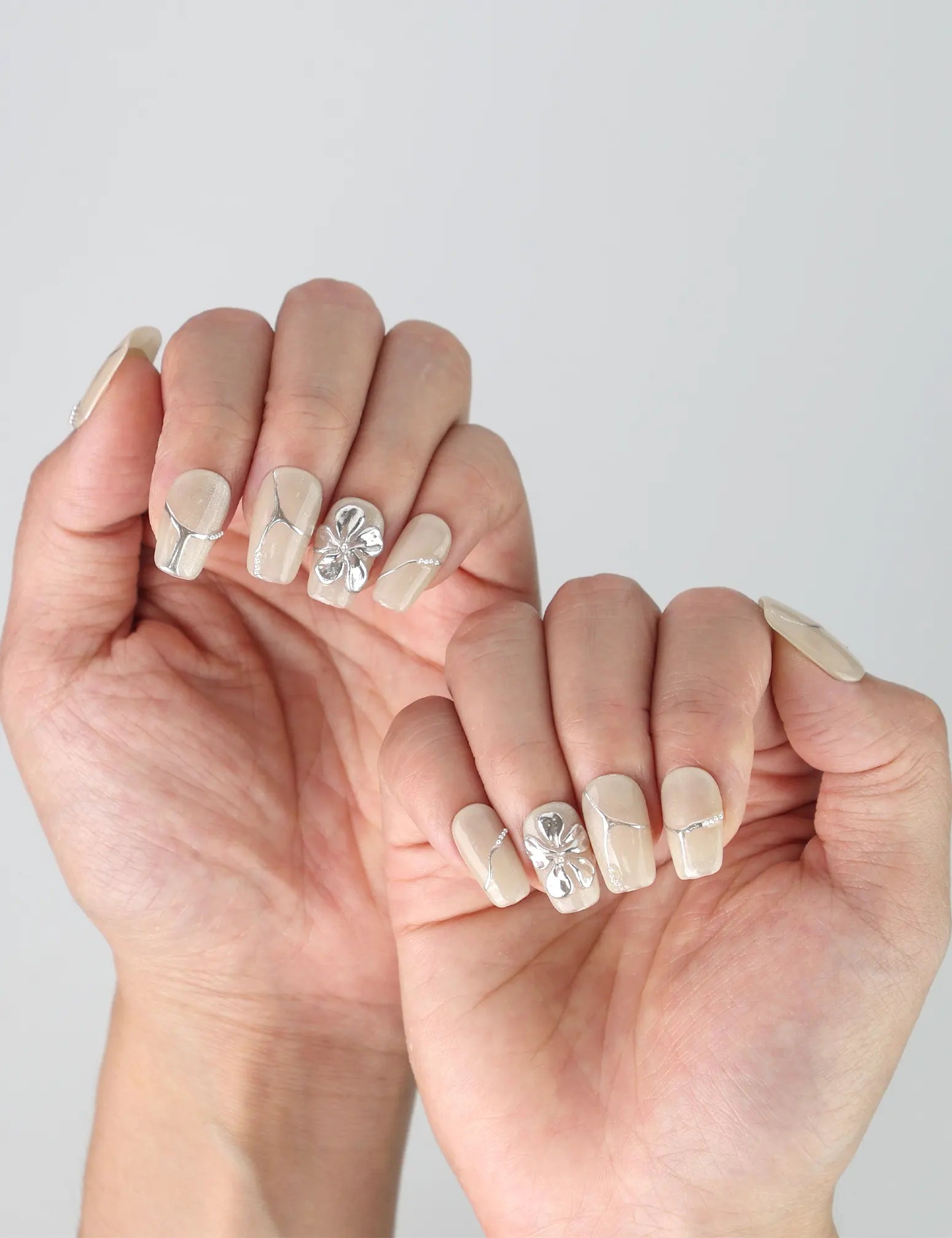 Side view of minimalist short square nails with subtle silver flower art on a clean ivory background