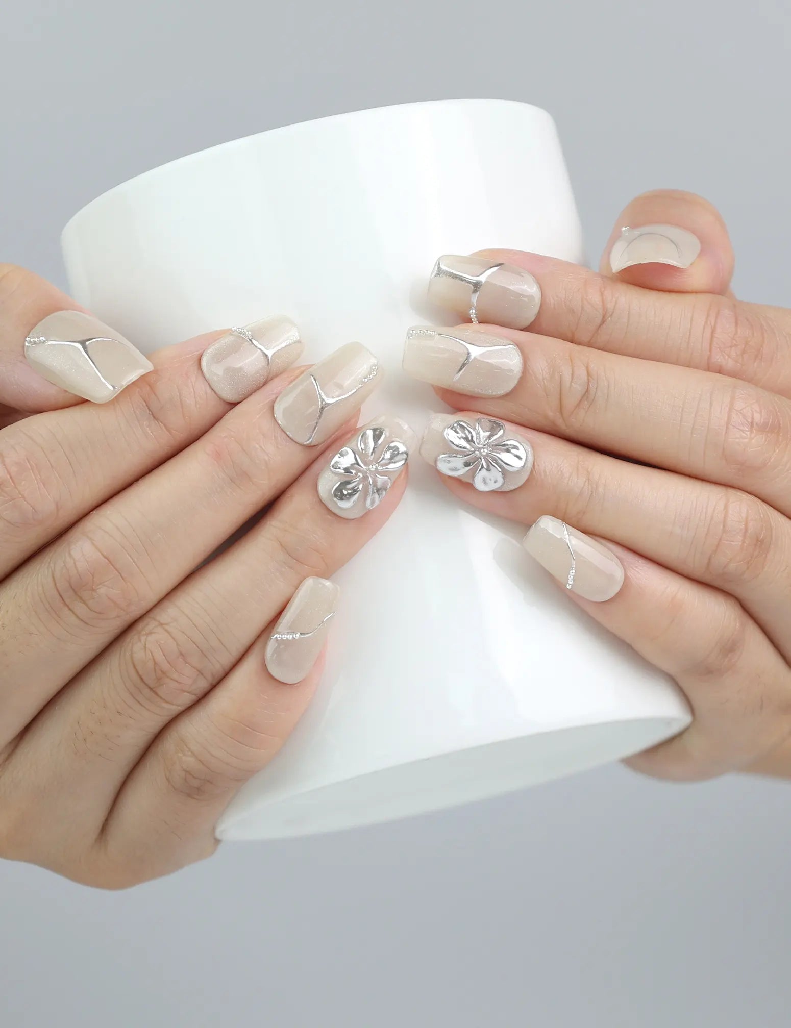 Hand holding a cup, showcasing Naillover’s ivory nails with elegant flower detailing in a modern square shape