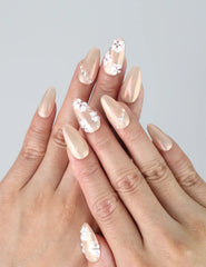 Hand model wearing pink almond press-on nails with shimmering base and detailed 3D flower accents