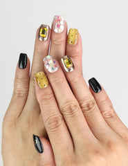 Hand wearing Luxe Mix Singapore press on nails in black, gold, and glitter with gem accents, naillover