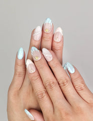 Hand wearing Naillover Marine Dream handmade press on nails with pastel colors, shimmering details, and delicate gold embellishments.