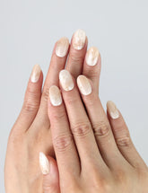 Hand model wearing short oval press-on nails in elegant greige with a soft golden shimmer finish