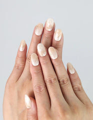 Hand model wearing short oval press-on nails in elegant greige with a soft golden shimmer finish