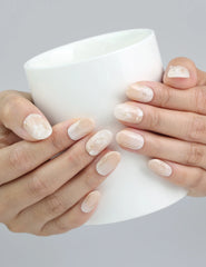 Hand holding a cup, showcasing Naillover’s everyday-friendly short greige nails with golden glow highlights
