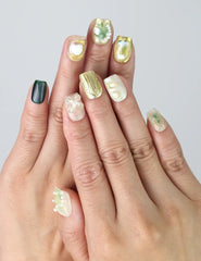 Hand model wearing short square press-on nails in mint green and white with gold foil and 3D flower details
