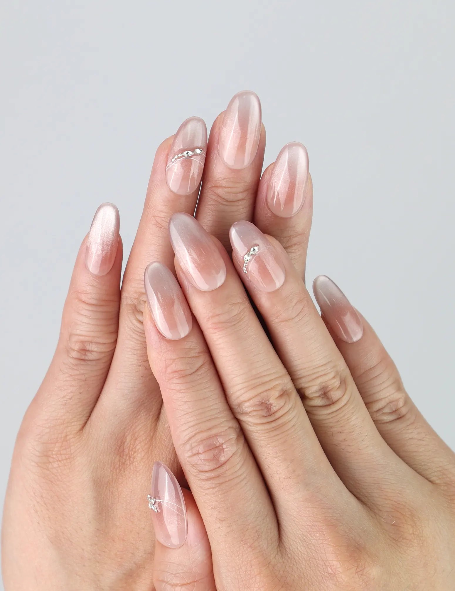 Hand model wearing medium oval press-on nails with soft shimmer gradient and delicate silver flower accents