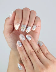 Close-up of Naillover handmade Clear Gleam nails in short square style, featuring white-grey marble and subtle gold shimmer.