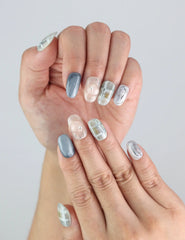 Hand model showcasing Naillover handmade press on nails with misty grey accents and classic grid designs.