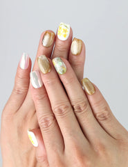 Hand wearing Naillover Nature's Glow press on nails with pastel floral prints and gold detailing for a soft, elegant effect.