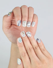 Model hands with Naillover Opal Whisper short handmade press on nails in elegant pastel grey and gold detail.