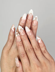 Close-up of Naillover Peach Petal handmade press on nails with nude and white base, 3D floral design, pearls, and gold accents.