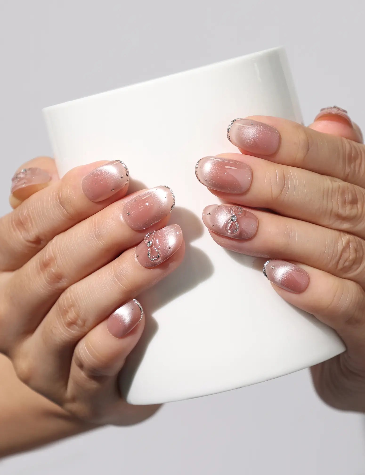 Holding a cup while wearing Sparkle Allure handmade cat eye gradient Singapore press on nails with silver bow accents by Naillover.