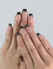 Close-up of hand wearing Naillover Nude Edge press on nails with black French tips and glossy nude gradient finish.