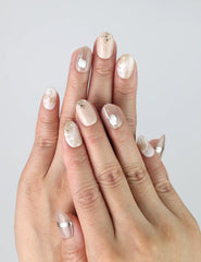 Hand model wearing short oval nude press-on nails with metallic gold accents and glossy finish