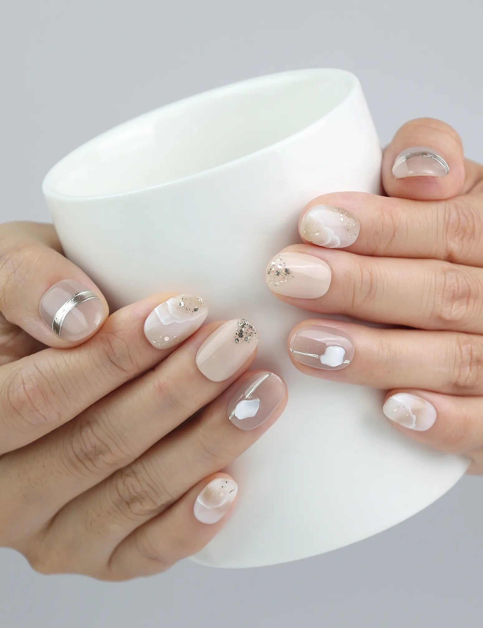 Hand holding a cup, showcasing Naillover’s short oval press-on nails in nude tones with gold sheen