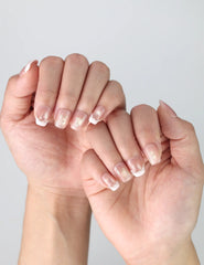 Fingers elegantly posed to showcase short press on nails in peach pink with linear gold accents and delicate sparkle by Naillover