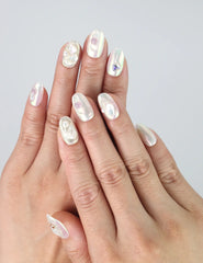 Hand model wearing short oval press-on nails with clustered rhinestones and pearl embellishments