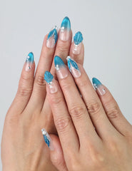 Hand wearing blue gradient almond press-on nails with shell-like texture and sparkling glitter, inspired by ocean beauty