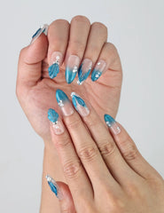 Close-up of handmade mermaid-inspired press-on nails with shimmering shell details and soft blue ombré tones