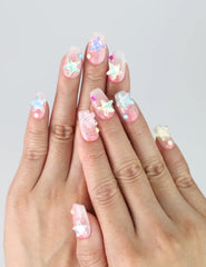 Hand model showing short coffin-shaped pink glitter press-on nails with 3D starfish charms in vibrant summer tones
