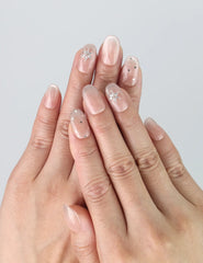 Hand model wearing nude short oval press-on nails with scattered glitter specks and clear crystal accents