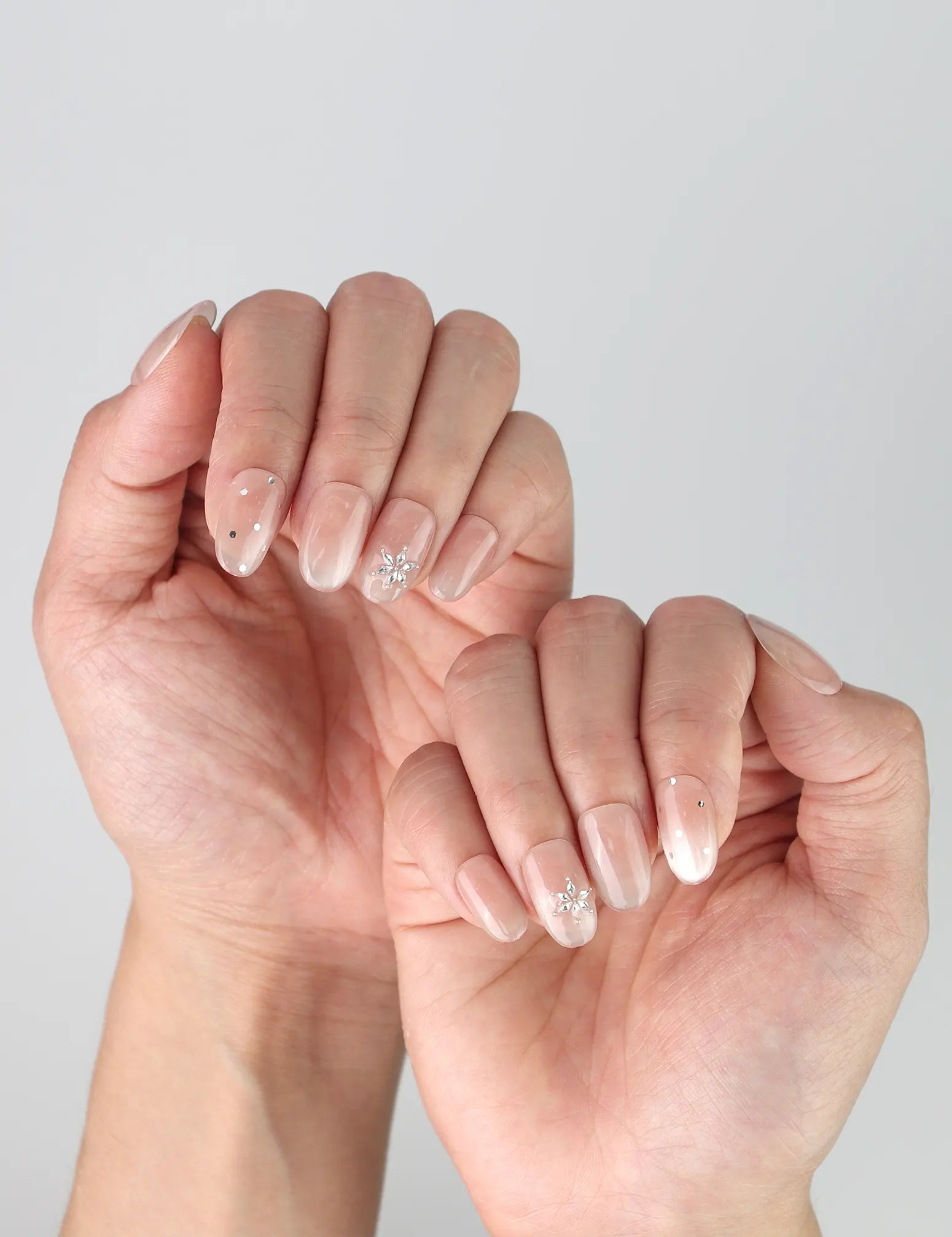 Side view of minimalist nude nails in short oval shape with monochrome speckled design and tiny rhinestones