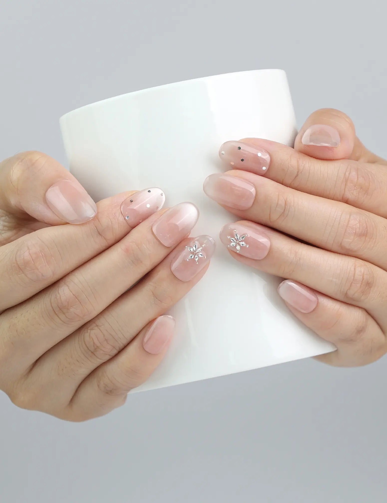 Hand holding a cup, showcasing Naillover’s short nude nails with natural speckled art and shimmering crystal details
